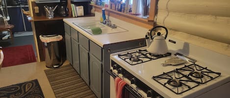 A compact kitchen with a gas stove, a sink, and cabinets.