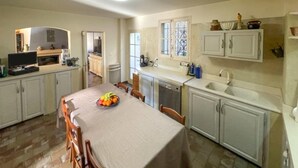 A compact kitchen with a dining area, featuring a table with fruit, a sink, and cabinets. - Nice home in La Roque-sur-Pernes (La Roque-sur-Pernes)