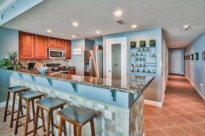A kitchen with a granite island, wooden bar stools, a stainless steel refrigerator, and a microwave.