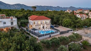 Ein zweistöckiges Haus mit Swimmingpool, umgeben von Grünpflanzen und Bergen im Hintergrund.