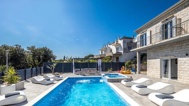 Ein Schwimmbad mit Liegestühlen, einer Pergola und Blick auf ein mehrgeschossiges Gebäude.