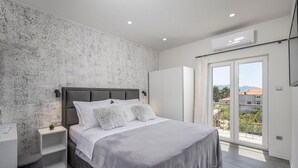 Ein modernes Schlafzimmer mit Bett, Nachttischen, einem Kleiderschrank und Blick durch eine Glastür.