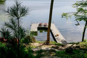 A wooden dock extending into calm water, with two chairs and a dog resting on it. - Stylish and Cozy Cabin on the Red Cedar Chain overlooking quiet bay (Birchwood)