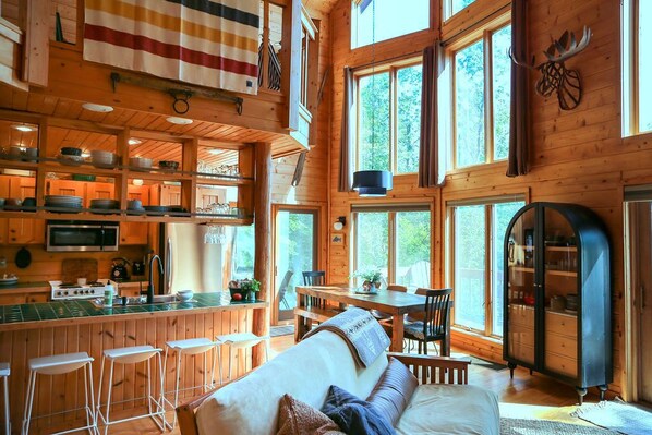 A spacious cabin with a large dining area, a cozy living room with a sofa, and a kitchen with wooden cabinets and a bar area. - Stylish and Cozy Cabin on the Red Cedar Chain overlooking quiet bay (Birchwood)