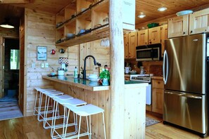 A wooden cabin kitchen with a stainless steel refrigerator, bar stools, and a wooden island. - Stylish and Cozy Cabin on the Red Cedar Chain overlooking quiet bay (Birchwood)