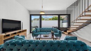 Uma sala de estar moderna com televisão de tela plana, sofás estofados em tons de verde-água, uma mesa de centro e uma escada.