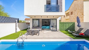 Uma casa moderna de dois andares com piscina, área de estar externa e entrada com porta de vidro.
