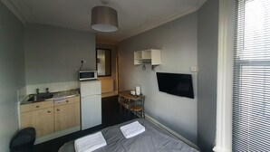 Habitación de hotel compacta con kitchenette, cama con toallas, una mesita pequeña y televisor montado en la pared.
