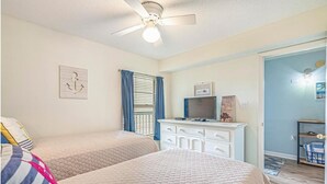 Une chambre avec deux lits, un ventilateur de plafond, une commode et un téléviseur.