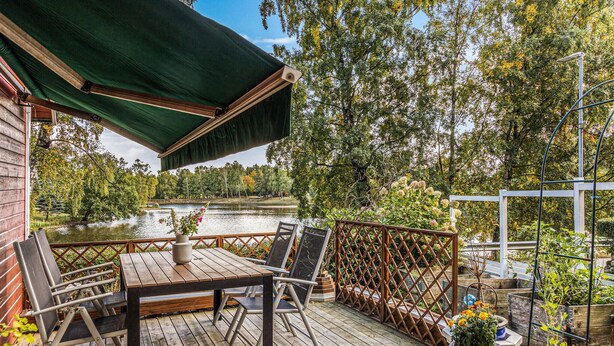Eine Holzterrasse mit Tisch und Stühlen, mit Blick auf einen See, umgeben von Bäumen.