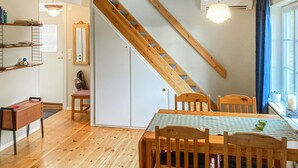 Ein Essbereich mit Holztisch und Stühlen, einer Treppe und einem Fenster mit Vorhängen.