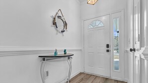 A hallway with a white door, a small table with decorative items, and a wall-mounted light fixture. - Beach House Fun Time (Wilmington)