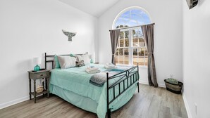 A bedroom with a bed, a nightstand, a window with curtains, and a ceiling fan. - Beach House Fun Time (Wilmington)