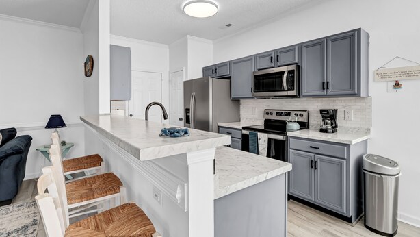 A modern kitchen with grey cabinets, a white countertop, and a stainless steel sink. - Beach House Fun Time (Wilmington)