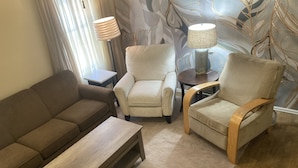 A living room with a brown sofa, two beige armchairs, a wooden coffee table, and two lamps on side tables.