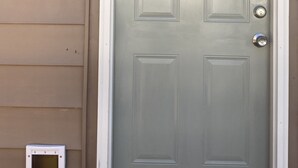 A light green door with a decorative glass panel above it, a metal door knocker, and a small vent on the wall to the left.