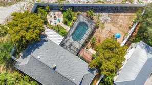 An aerial view of a residential property with a swimming pool, patio, and surrounding vegetation.