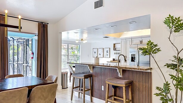 A modern kitchen with a bar area, a dining table with chairs, and a potted plant. - Palma Sola Getaway | Private Pool + Games (Bradenton)