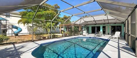 Una piscina con zona sombreada, sillas de descanso y un tobogán.