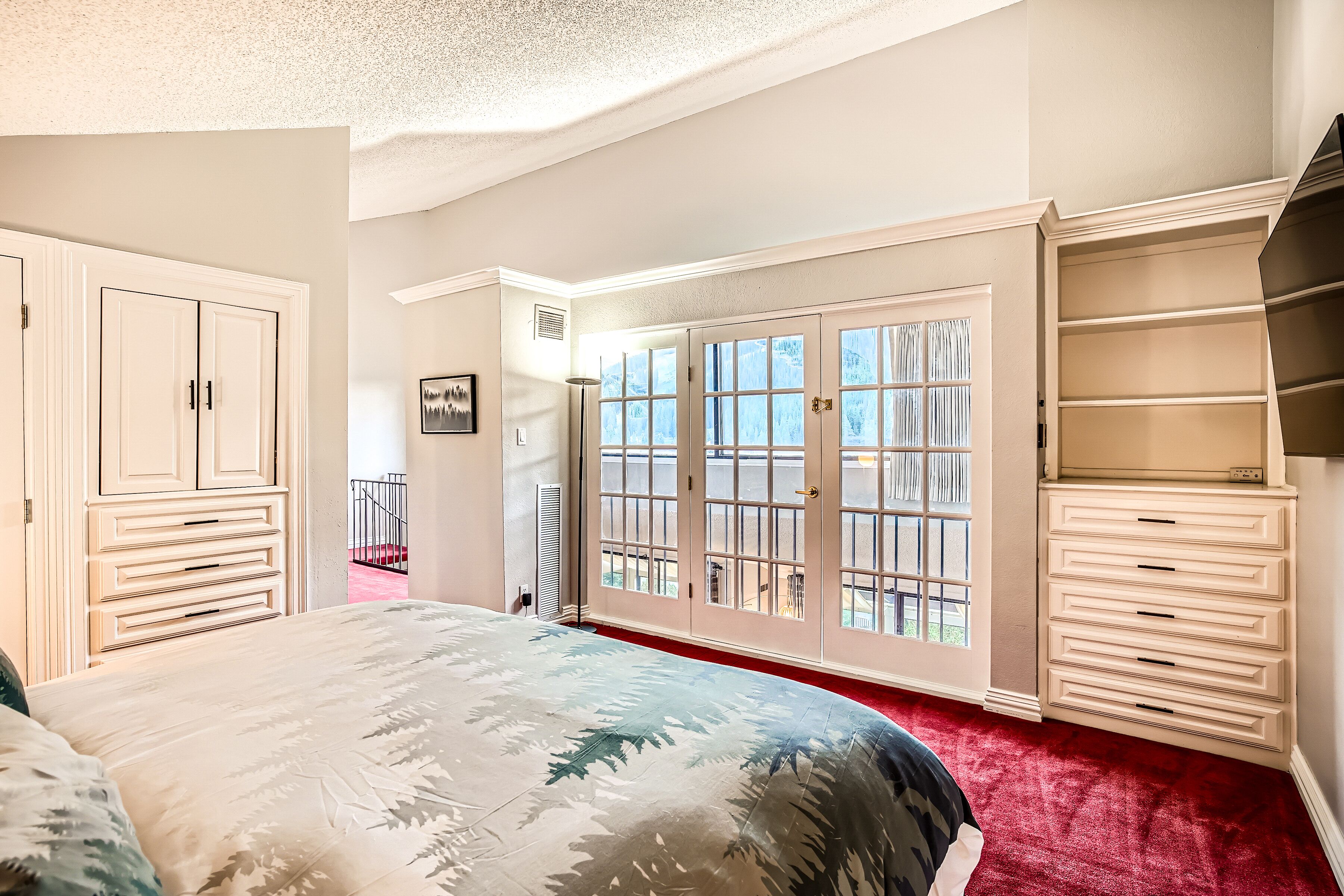 Une chambre à coucher avec un grand lit, une armoire, une commode et une porte-fenêtre coulissante donnant sur un balcon.