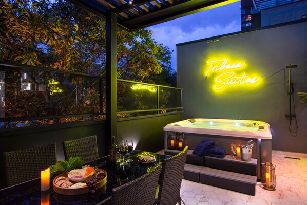 An outdoor seating area with a glass table, wicker chairs, a neon sign for 'Tribe Suites', a hot tub, and a tiki bar. - Luxury 8BR Villa with Rooftop and Jacuzzis on Lleras Park (Medellín)