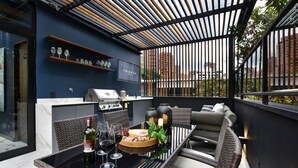 Een terras buiten met een barbecue, zitplaatsen en een bar, compleet met glazen en flessen.
