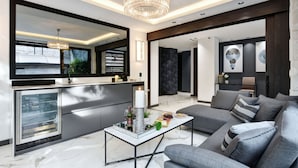 Een moderne woonkamer met een grijze bank, een salontafel en een keukenhoek met een koelkast en een spoelbak.