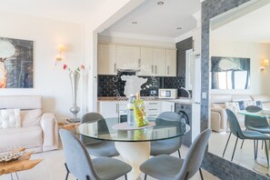 Une cuisine moderne avec des carreaux noirs et blancs, un coin repas avec une table en verre et des chaises grises, et un salon avec un canapé blanc.