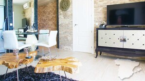 En moderne stue med en murstensvæg, et fladskærms-tv, hvide møbler og et træsofabord.