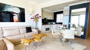 En moderne stue med en beige sofa, et træbord og et spiseområde med hvide stole og et glasbord.