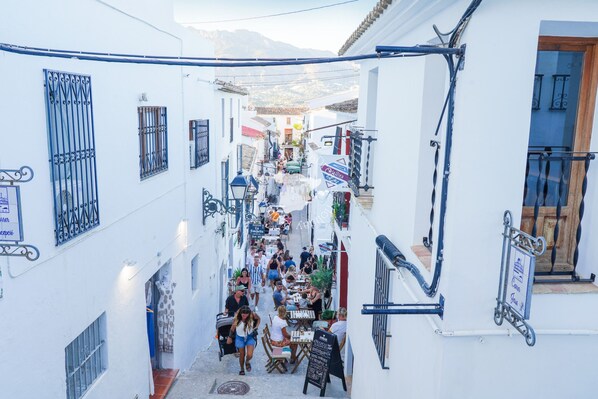 A narrow street with white buildings, outdoor seating, and a signboard.