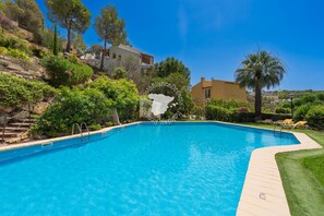 A swimming pool with a wooden deck, surrounded by greenery and a hillside.