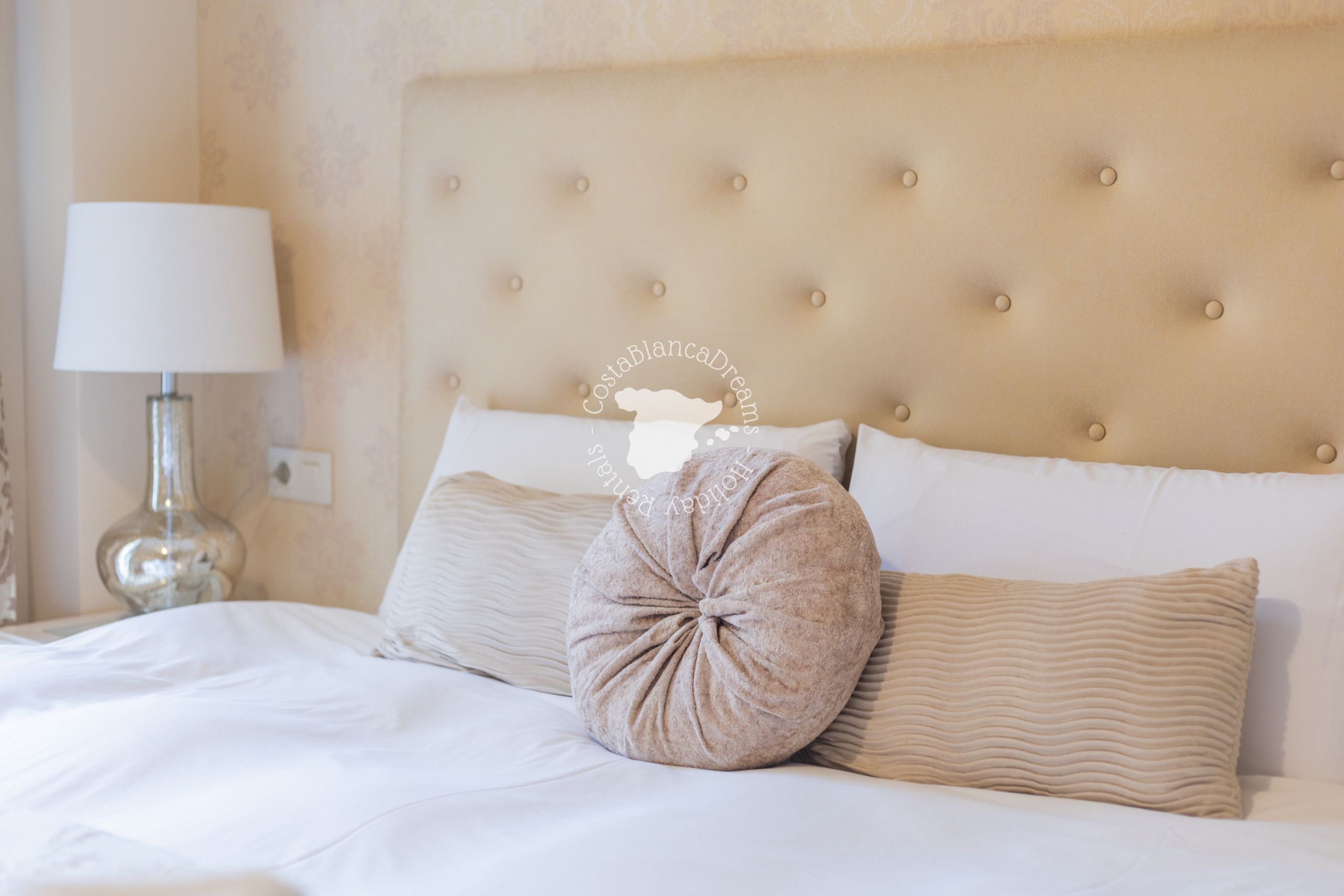 A neatly made bed with a tufted headboard, a lamp, and a decorative pillow.
