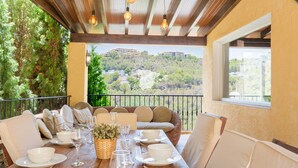Uma área de jantar com mesa de madeira posta para refeição, rodeada por assentos acolchoados, e vista para uma encosta.
