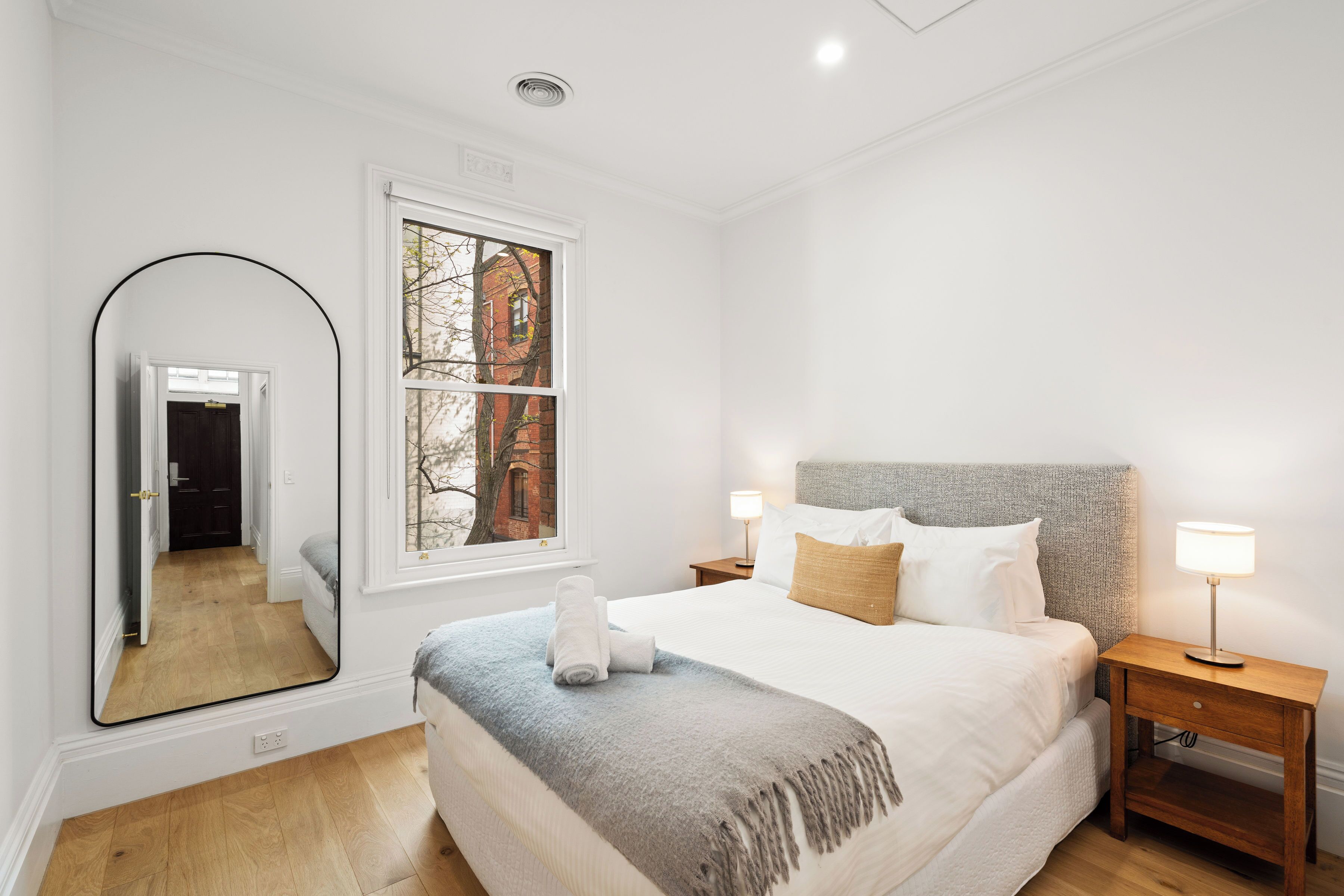 Camera da letto con un letto grande, un comodino, uno specchio e una finestra con vista su un edificio.