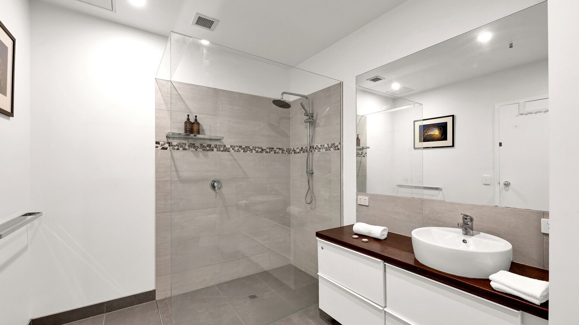 A modern bathroom with a glass-enclosed shower, a large mirror, and a white sink with a wooden countertop.