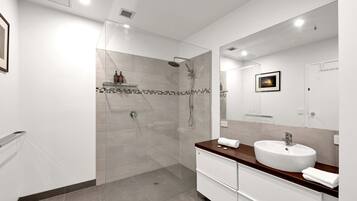 A modern bathroom with a glass-enclosed shower, a large mirror, and a white sink with a wooden countertop.