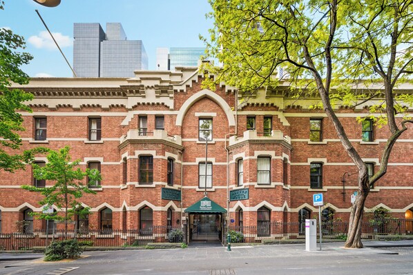 A historic brick building with a central entrance, a green awning, and a parking sign. - Gordon House Apartments (Melbourne)