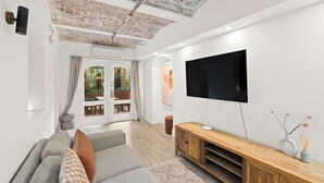 Uma sala de estar moderna com uma grande televisão de tela plana, um console de madeira e um sofá cinza com almofadas estampadas.