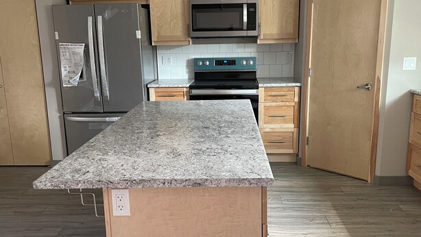 Una cocina con armarios de madera, encimera de granito, refrigerador de acero inoxidable, microondas y horno.