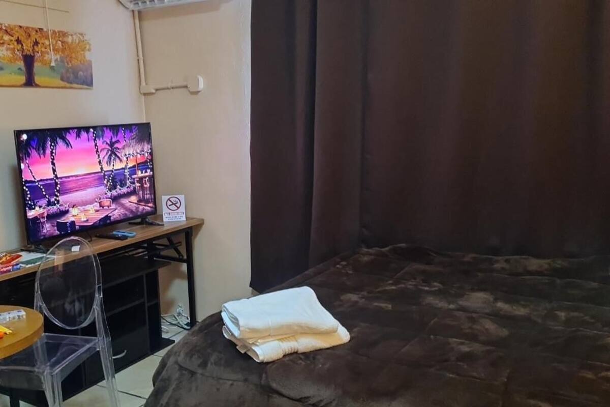 Una habitación con una cama, un televisor en un escritorio, una silla y una colcha sobre la cama.