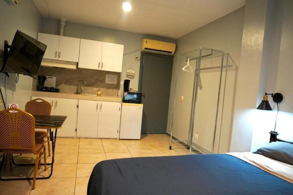 Una habitación compacta con cama, mesa de comedor con sillas, kitchenette, televisor montado en la pared y tendedero.