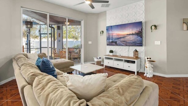 Un salón con un sofá color beige, una mesa de centro, un televisor y un ventilador de techo.