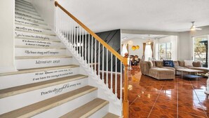 Una escalera con citas motivacionales, un salón moderno con un sofá y una mesa de centro, y un ventanal que proporciona luz natural.