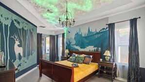 Un dormitorio con cama, mesitas de noche, una araña y un mural con motivos forestales en la pared.