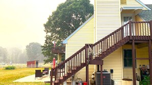 Une maison à deux étages avec un escalier brun menant à un balcon, une antenne parabolique et un grand climatiseur installé au rez-de-chaussée.