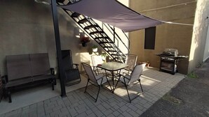 En udendørs terrasse med bord, stole, grill og trappe.