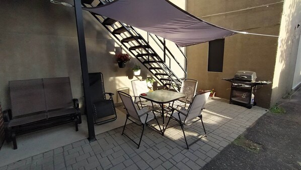 An outdoor patio with a table and chairs, a barbecue grill, and a staircase.