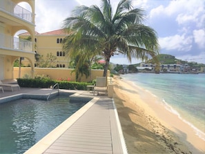 Ein Pool im Resort mit Holzterrasse, einer Palme und Blick auf den Strand.