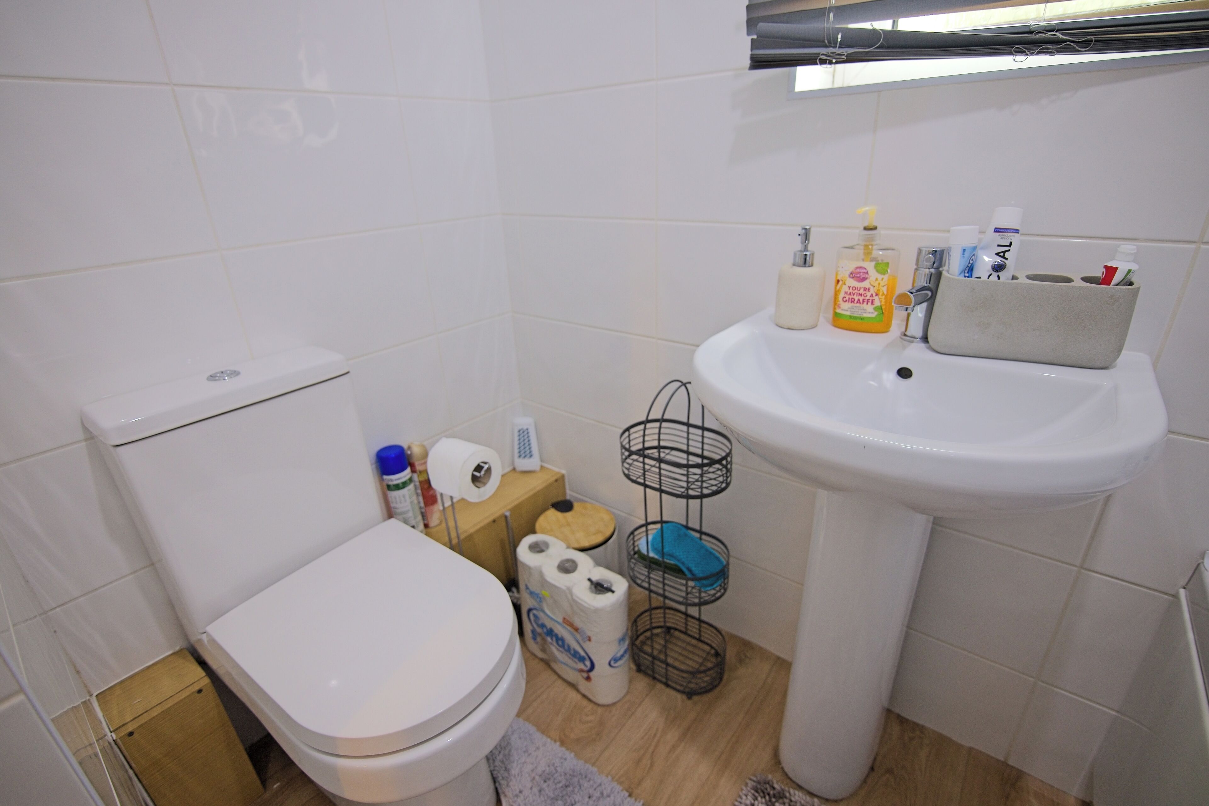 A small bathroom with a toilet, sink, and storage shelves.